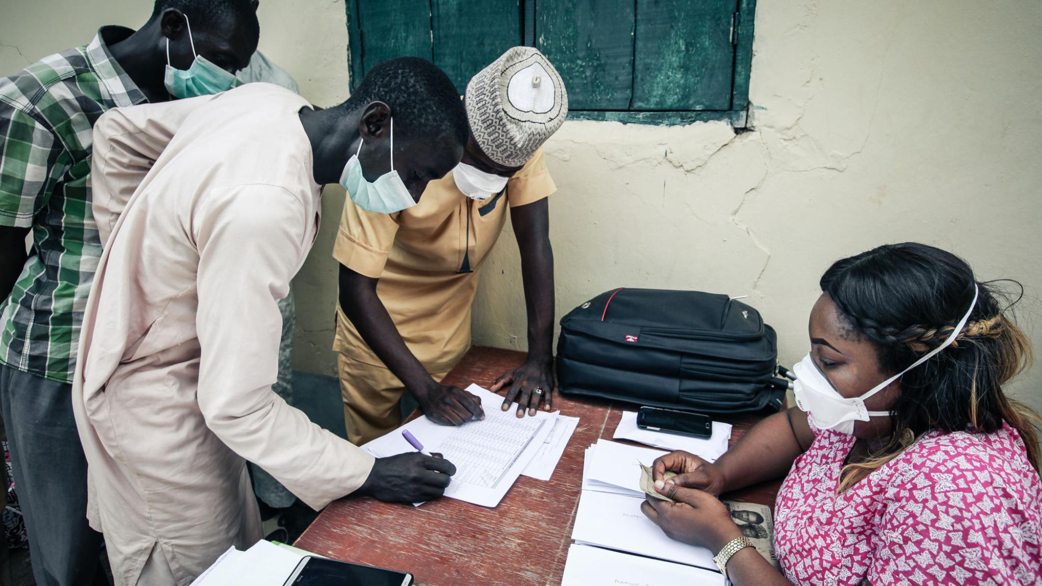 Two nigerian men in traditional clothes wearing facemasks in registry at health center